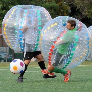 Two men playing bubble-ball soccer on a grass field