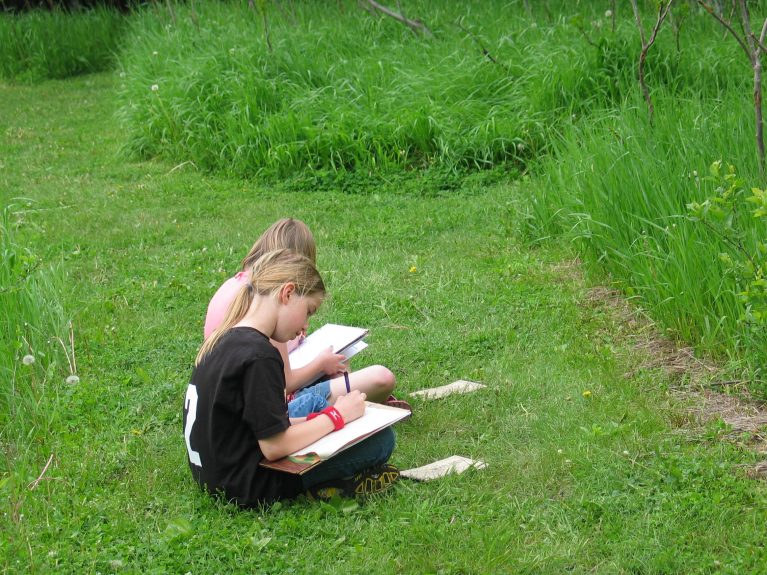 Two students sit drawing in the grass