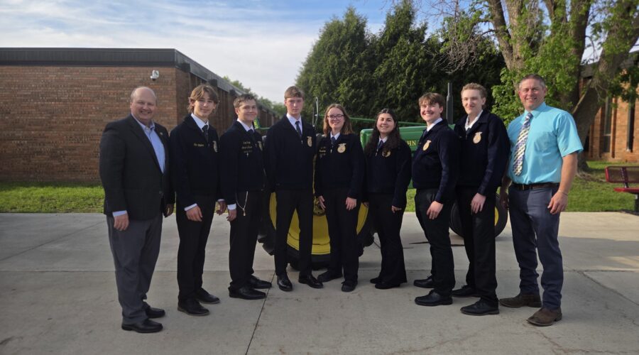 Seven members of the FFA Leadership team pose with Superintendent Matt Hillmann and FFA Advisor T.J. Austin in front of a John Deere tractor.