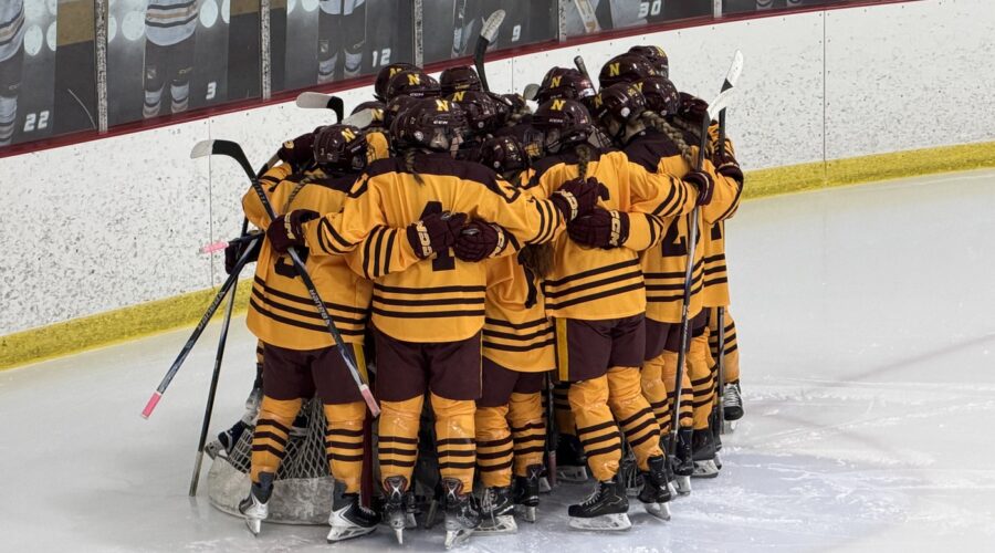 The NHS Hockey team is huddled together with their backs facing toward the camera.