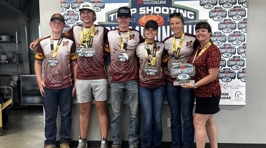 The first place Northfield High School Trap Team at the Alexandria tournament. Five students wearing medals stand with the coach who holds a trophy.