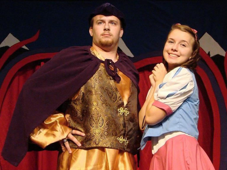 A man and woman dressed in costume pose on a stage for a production of Snow White