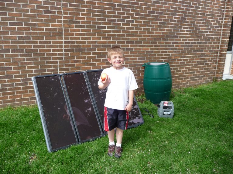 A boy smiles next to a solar panel